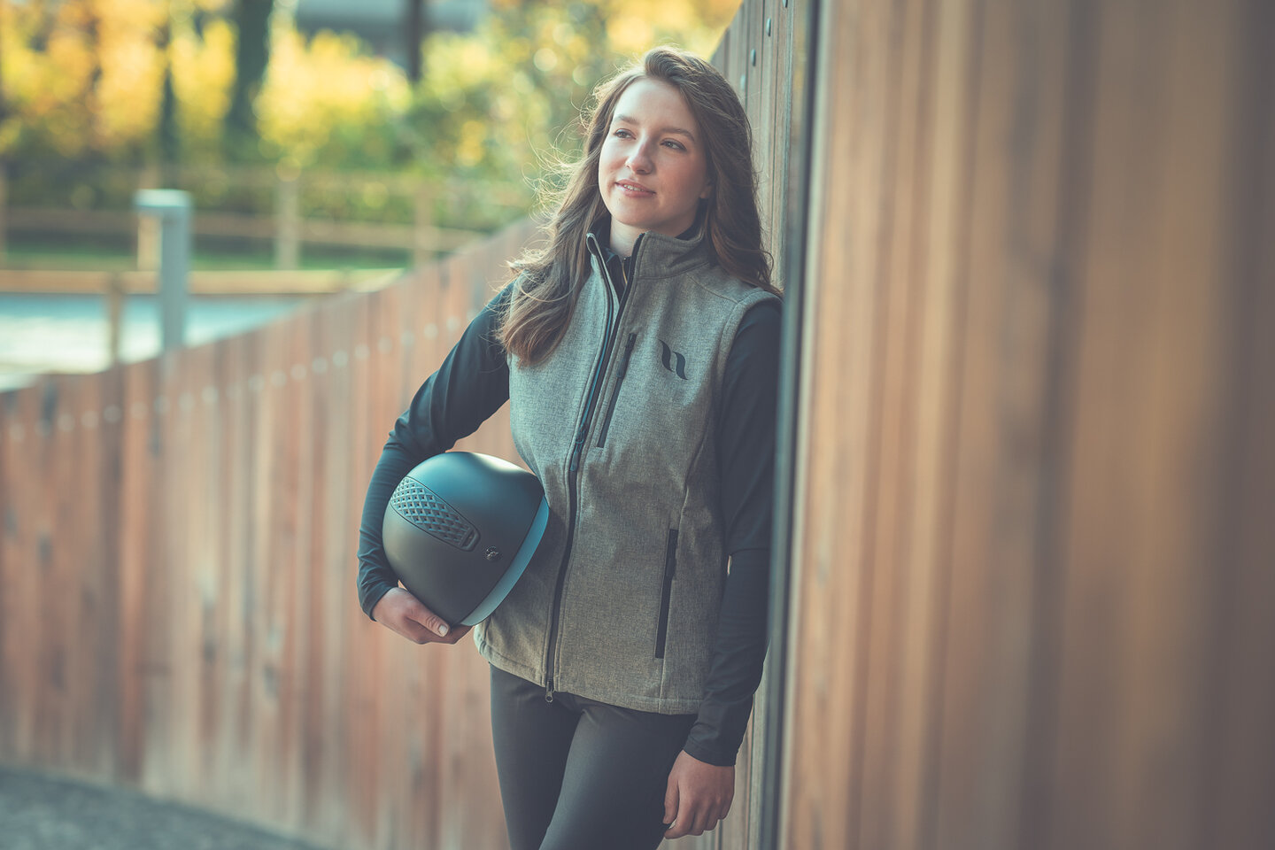model nikita showt kleding en veiligheidshelm van back on track en leunt tegen een houten wand